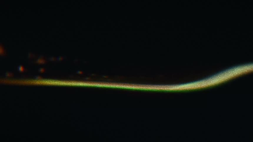 Pixelated lights of various colors flow over greenish curve against black background