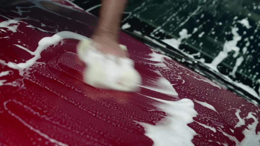 A person washing a vehicle with a sponge water and soap