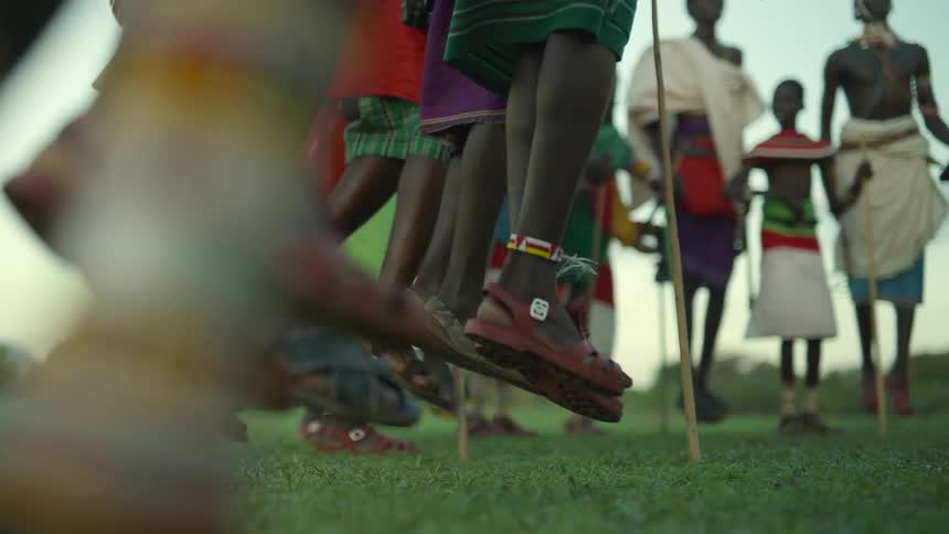 A tribe of boys and men stand in a circle and jump up and down