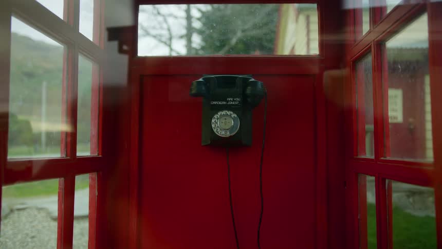 A vintage style rotary phone sits inside a red phone booth