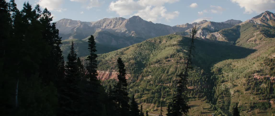 Mountain range under a cloudy sky is seen through trees