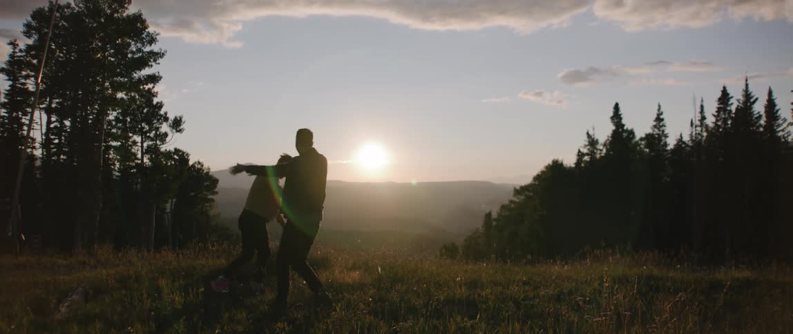 Two men play around on the field at sunset