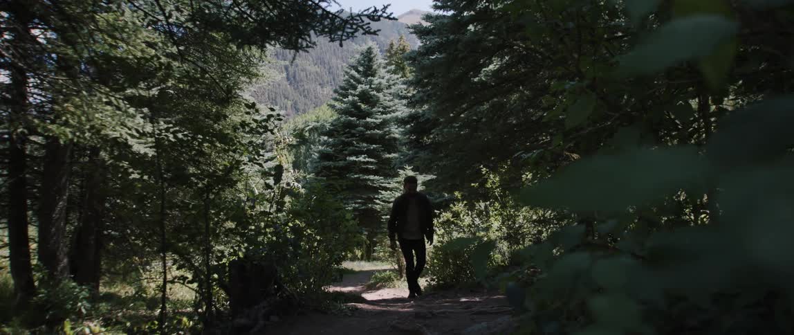 A man is walking on a dirt trail in the woods and looking around
