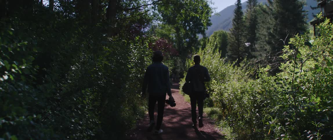 Two people that are walking down a trail in a forest