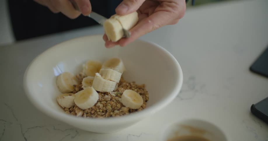 Young man slices a banana over cereal inside a bowl for breakfast