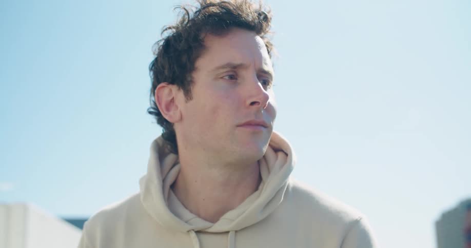 Man wearing a hoodie sitting outdoors typing on a laptop