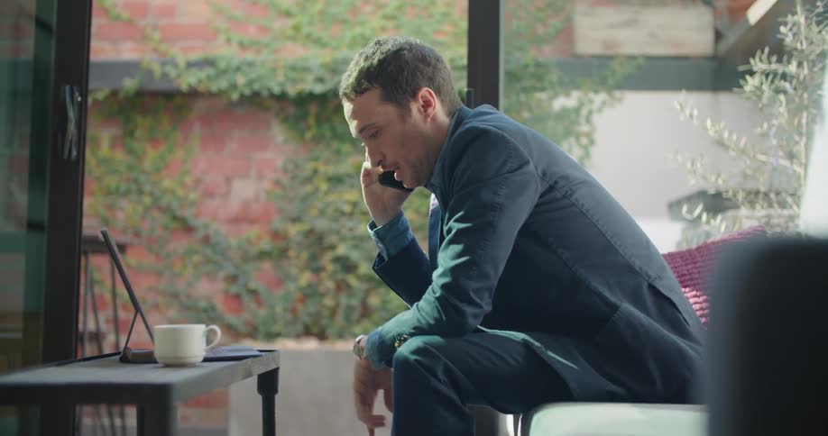 Man sitting on a couch in the living room near the patio talking on a smartphone