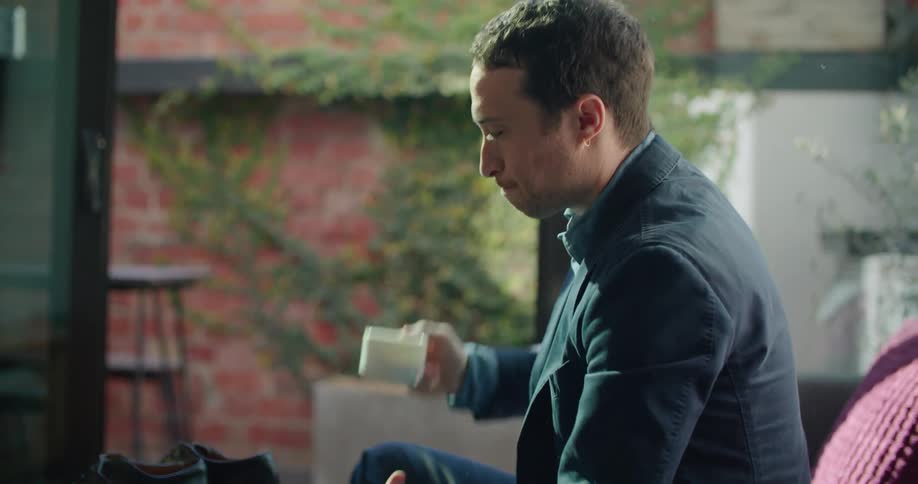 A man sits his shoes on a table and drinks coffee from a mug