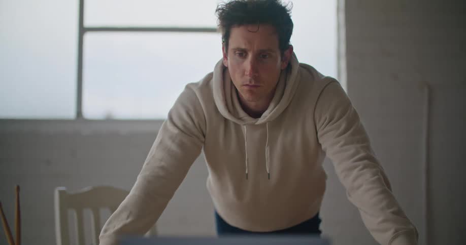Man wearing a sweater waiting in front of a laptop over a desk