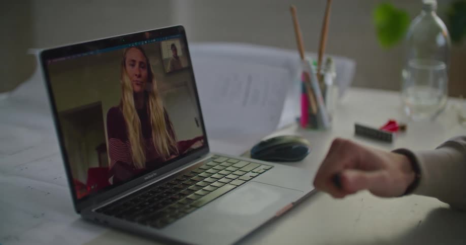 A man sits at a desk having a video call with a woman on a laptop