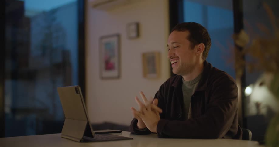 A man sits at a table having a video call on a tablet