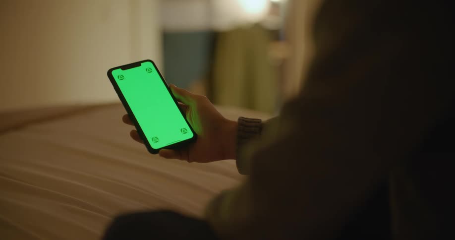 Man sitting on a bed at home using a smartphone with a green replaceable screen