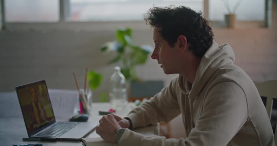 Young man sitting at a desk talking to someone on a video call on a laptop