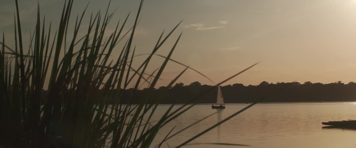 A lone sailboat is moving slowly on a lake at dusk