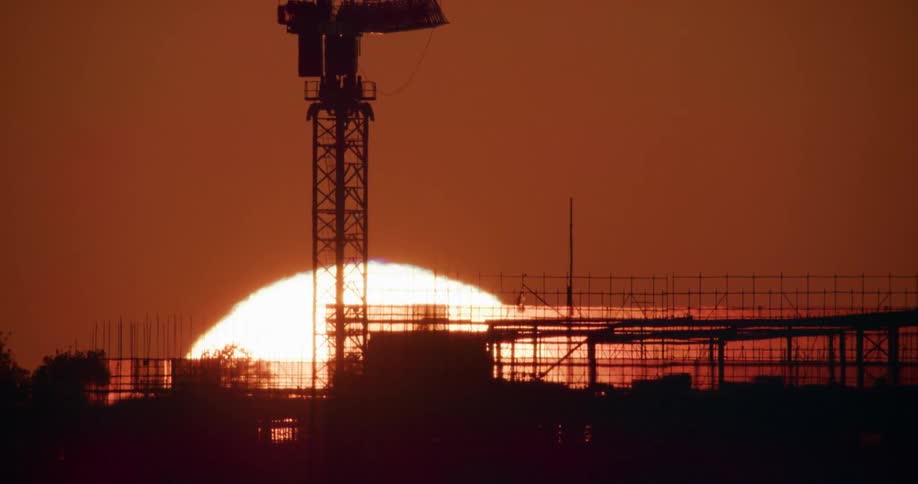 Large sun rises on horizon in red sky backlighting tower flag and metal framework