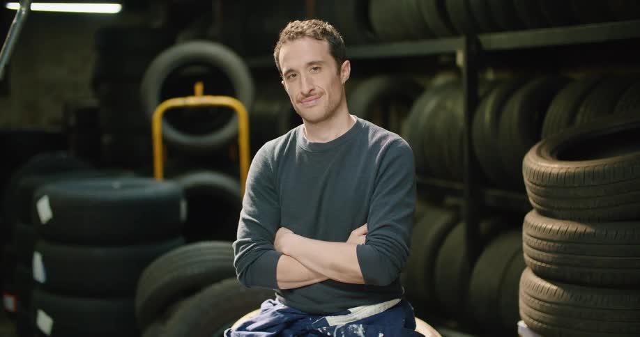 Young man sitting over a pile of tires inside a warehouse smiling at the camera