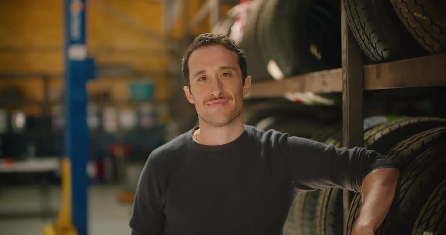 A man leans against tires in the auto shop