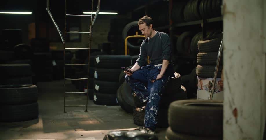 An employee sitting on tires while texting