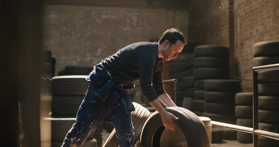 A mechanic chooses a tire from a large room and gives it a jiggle