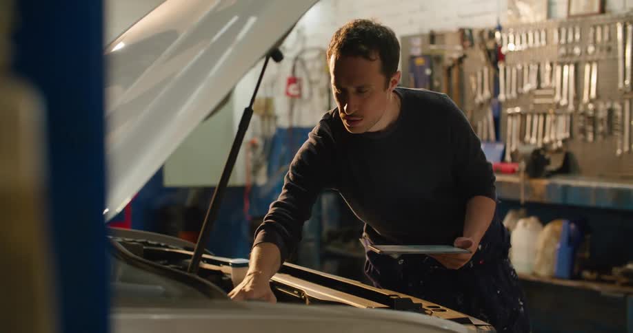 A mechanic is checking an engine and using a tablet