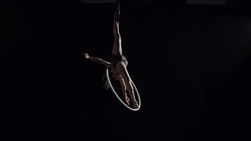 A woman spinning on a suspended hoop while doing acrobatics in the air