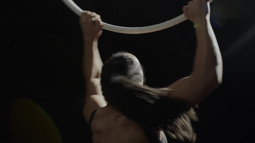 Female gymnast walks up to suspended hoop and grapes it before spinning and starting routine