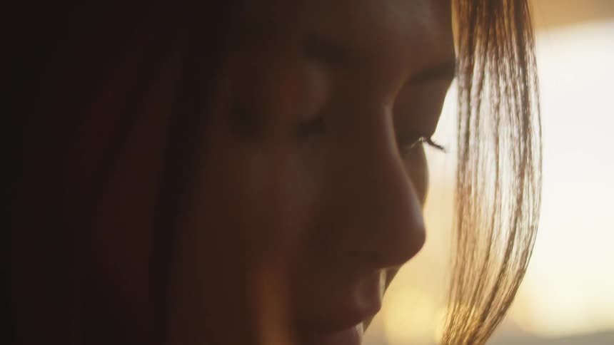 A woman texts on her smartphone while standing next to a window at home