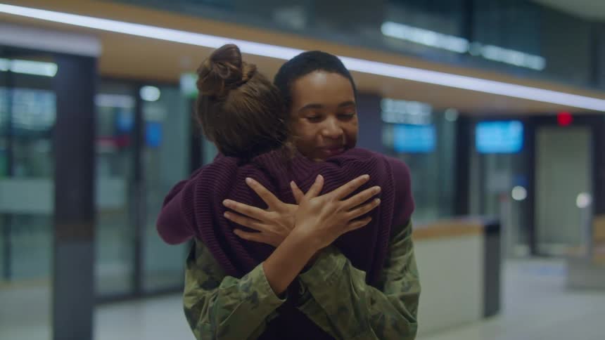 Young girl greets a friend wearing military unform with a hugh outside an airport