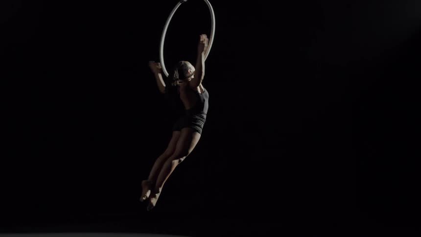 An aerial acrobat spinning on a ring by the back of her neck before landing