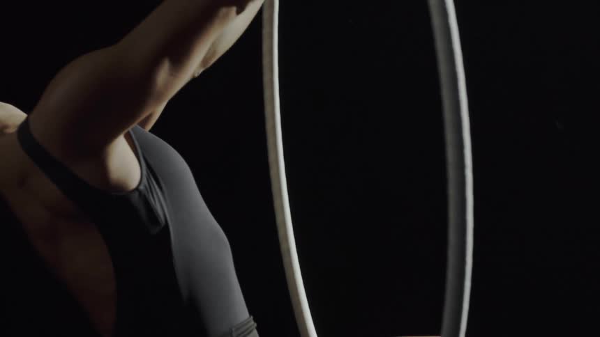A woman in a room hanging on a gymnast ring with a wall in the background