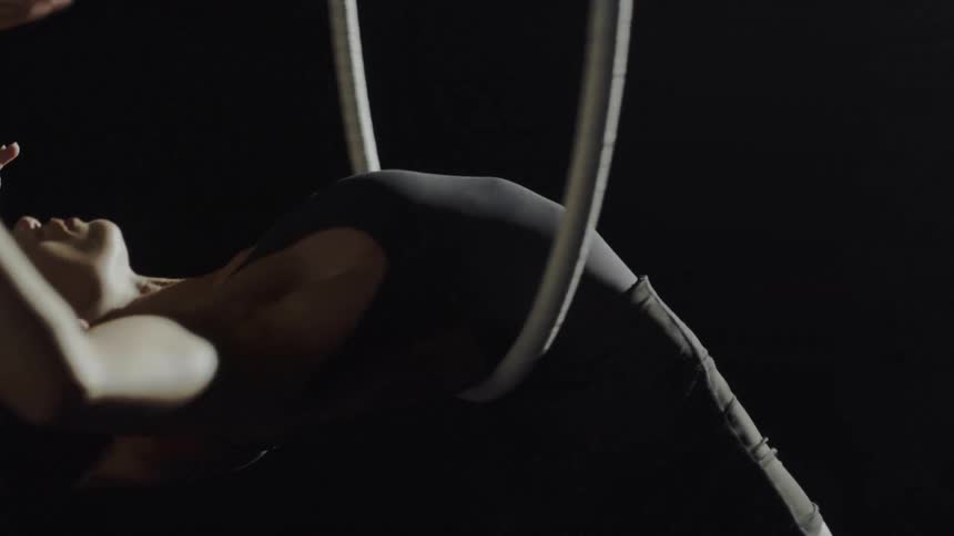 A woman in a room hanging on a gymnast ring with a wall in the background