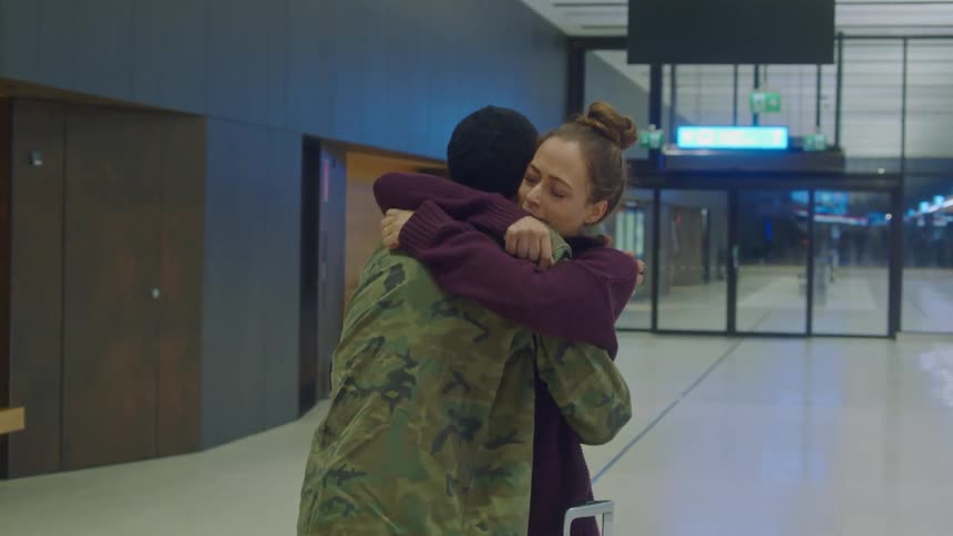 A woman grabs and hugs a man in a military uniform tightly in a transportation center