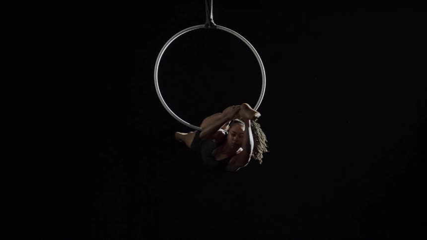 Strong fit muscular woman doing acrobatics hanging from a ring