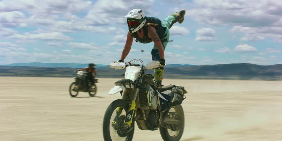 People are doing tricks on dirt bikes as they ride in the desert