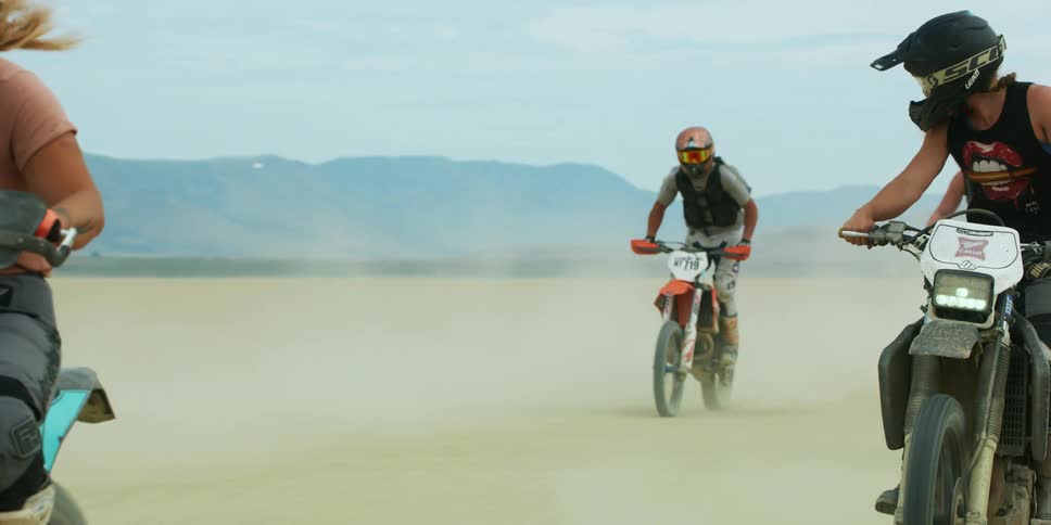 A man does a pop wheelie while racing a dirt bike