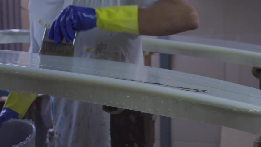 A male employee applying a coating to surfboards in a place of business