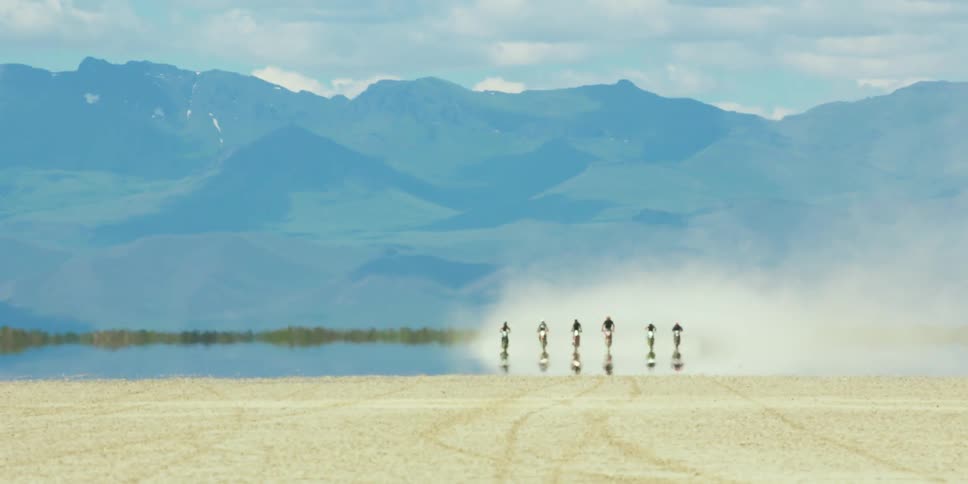 A group of motorcycles moves across a desert
