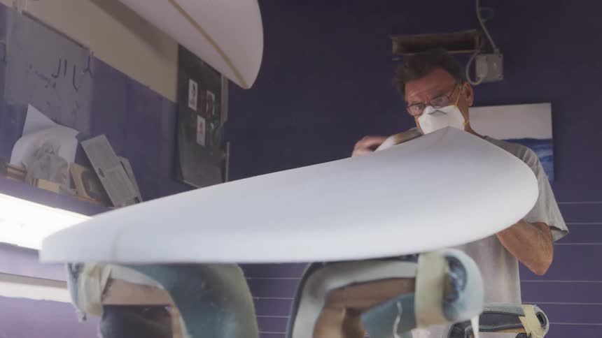 A man is sanding a new surfboard