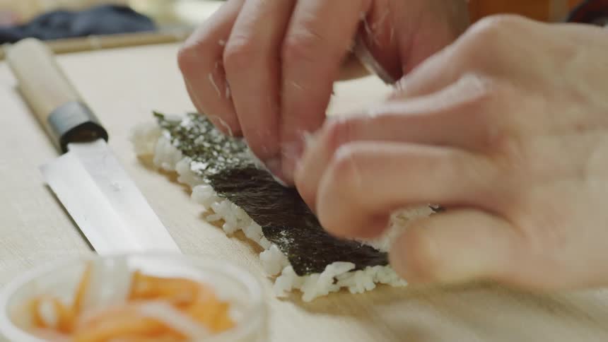 Cook preparing a roll of sushi over a table in a restaurant