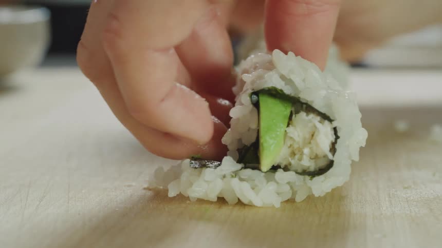 Hands are rolling up fresh sushi on a wooden counter