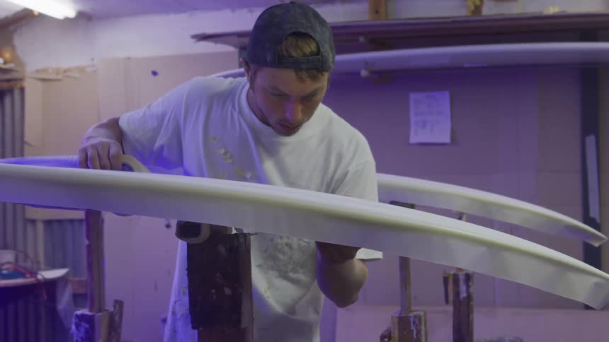 A man smothing tape onto a surfboard in a place of business