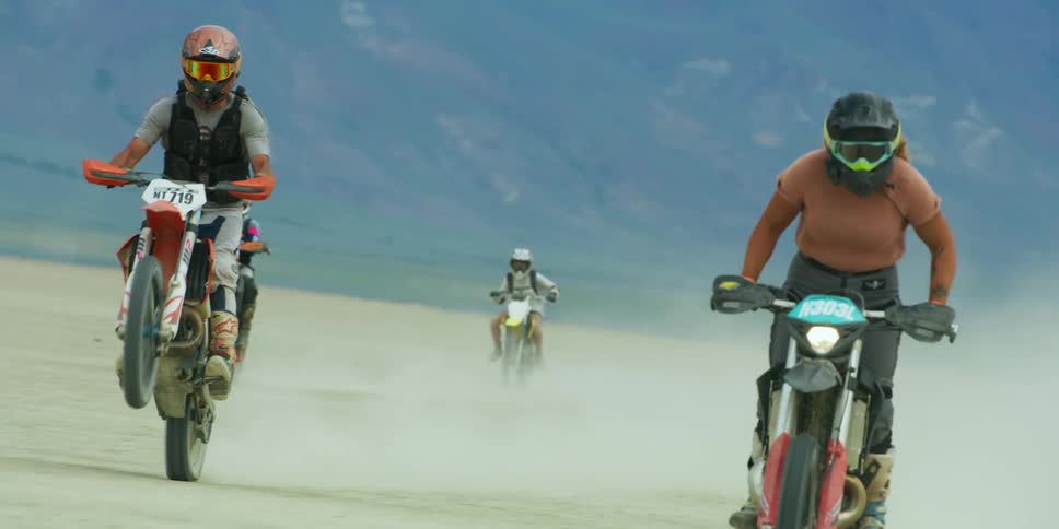 A group of people ride dirt bikes in a desert area