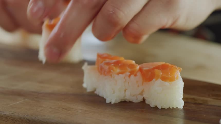 A sushi chef lines pieces of sushi on a wood platter