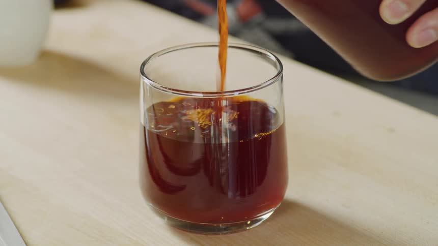 A person pours a brown liquid into a glass