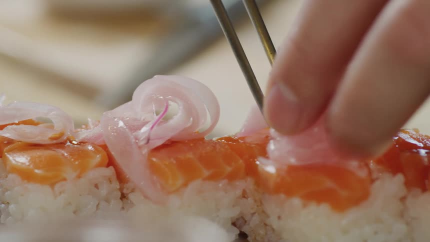 A sushi chef uses chopsticks to place pickled radish on salmon sushi