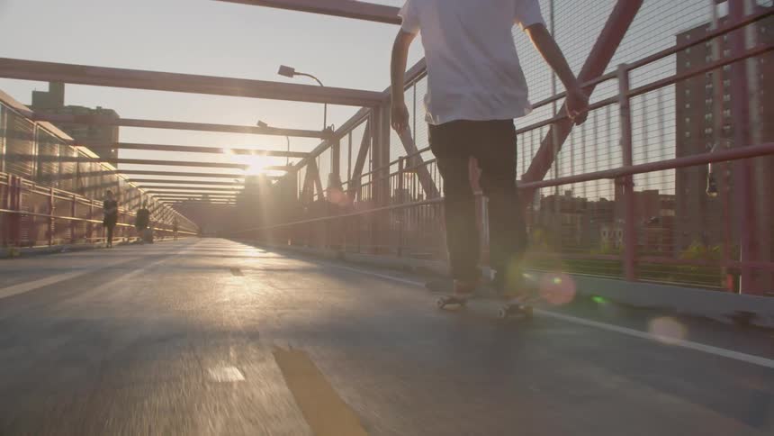 People ride bikes and skateboards over a bridge at sunset