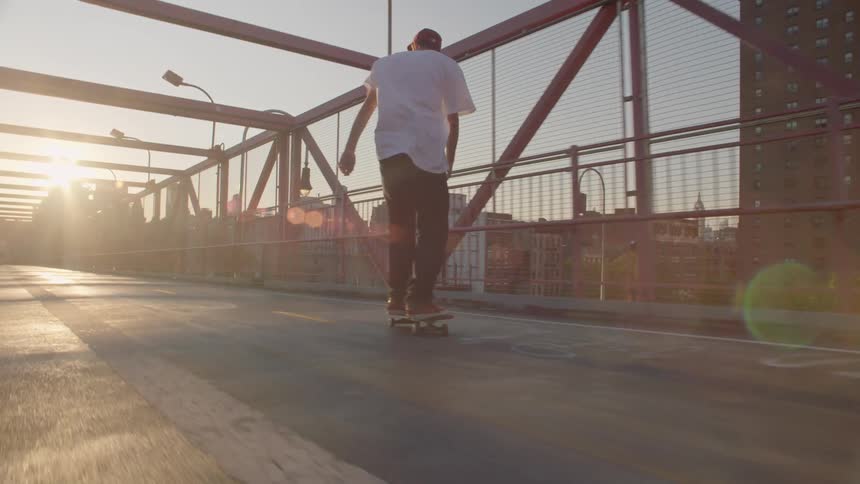 A man is skateboarding on a bridge at sunset
