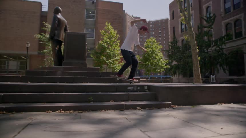 A skateboard flips his board up on a raised concrete platform that holds a statue