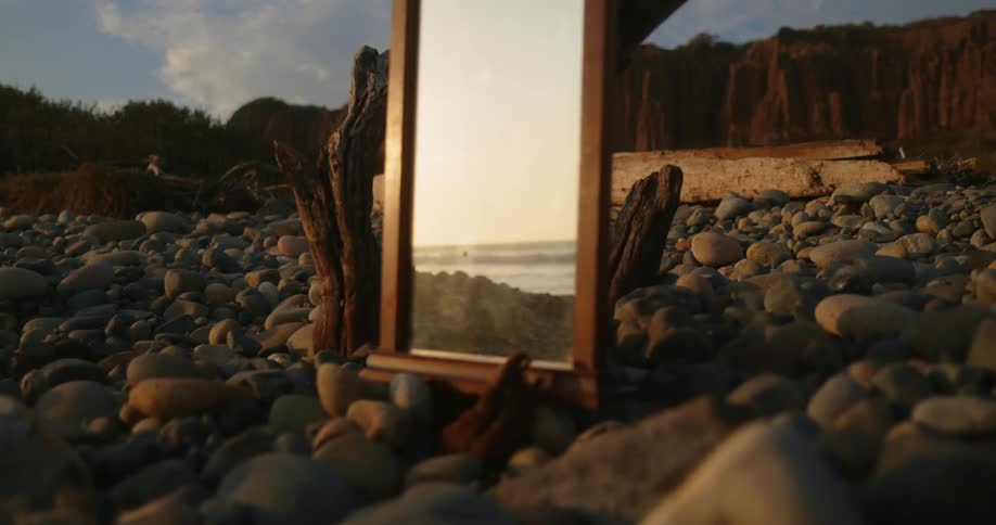 Reflection of a beach on a mirror resting over the rocks in the coast at sunset