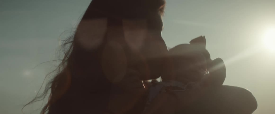 Mother holds and kisses baby girl as they stand outside under the sun